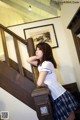 A woman in a school uniform leaning against a staircase.