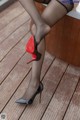 A woman in black stockings and red high heels sitting on a wooden deck.