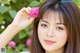 A woman holding a pink flower in front of her face.