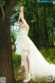 A woman in a white dress standing next to a tree.