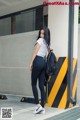 A woman in a white shirt and black leggings leaning against a wall.