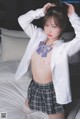 A woman in a white shirt and plaid skirt posing on a bed.