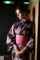 A woman in a black and pink kimono leaning against a wall.