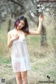 A woman in a white lingerie holding a branch of a tree.