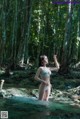 A woman in a bikini standing in a stream in the woods.