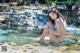 A woman in a bikini sitting on a rock in the water.