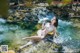 A woman in a bikini laying on a rock in the water.