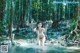 A woman in a bikini standing in a stream in the woods.