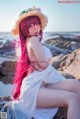 A woman with pink hair sitting on a rock by the ocean.