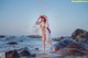 A woman in a white bikini standing on rocks in the ocean.