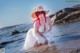 A woman in a white dress and a straw hat sitting in the water.