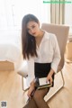 A woman sitting on a chair holding a book and pen.