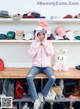 A woman sitting on a bench in front of a shelf of hats.