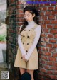 A woman leaning against a brick wall wearing a trench coat.