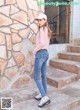 A woman standing in front of a stone wall wearing a pink shirt and jeans.