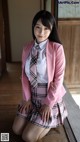 A woman in a pink jacket and plaid skirt posing for a picture.