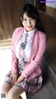 A woman in a pink jacket and plaid skirt posing for a picture.