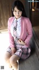 A woman in a pink jacket and plaid skirt posing for a picture.