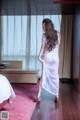 A woman in a white dress standing in a hotel room.