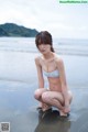 A woman in a bikini crouching on the beach.