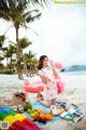 A woman sitting on a beach next to a pink flamingo.