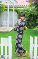 A woman in a kimono standing in front of a white fence.