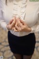 A woman in a white shirt and black skirt holding her hands together.