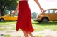 A woman in a red skirt is walking towards a yellow car.