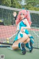 A woman with pink hair sitting on a tennis court.